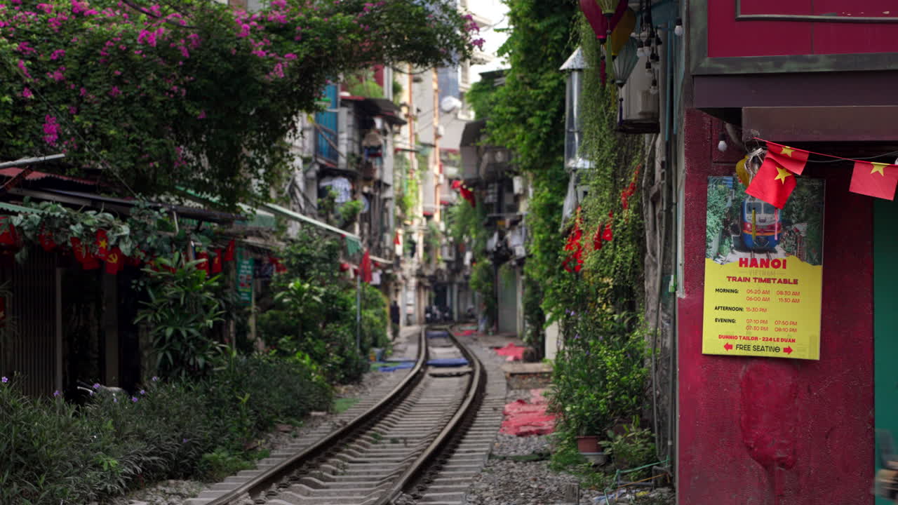 Locals and tourists cross Train Street walking and driving over the tracks connecting the city, beautiful flowery vegetation, static