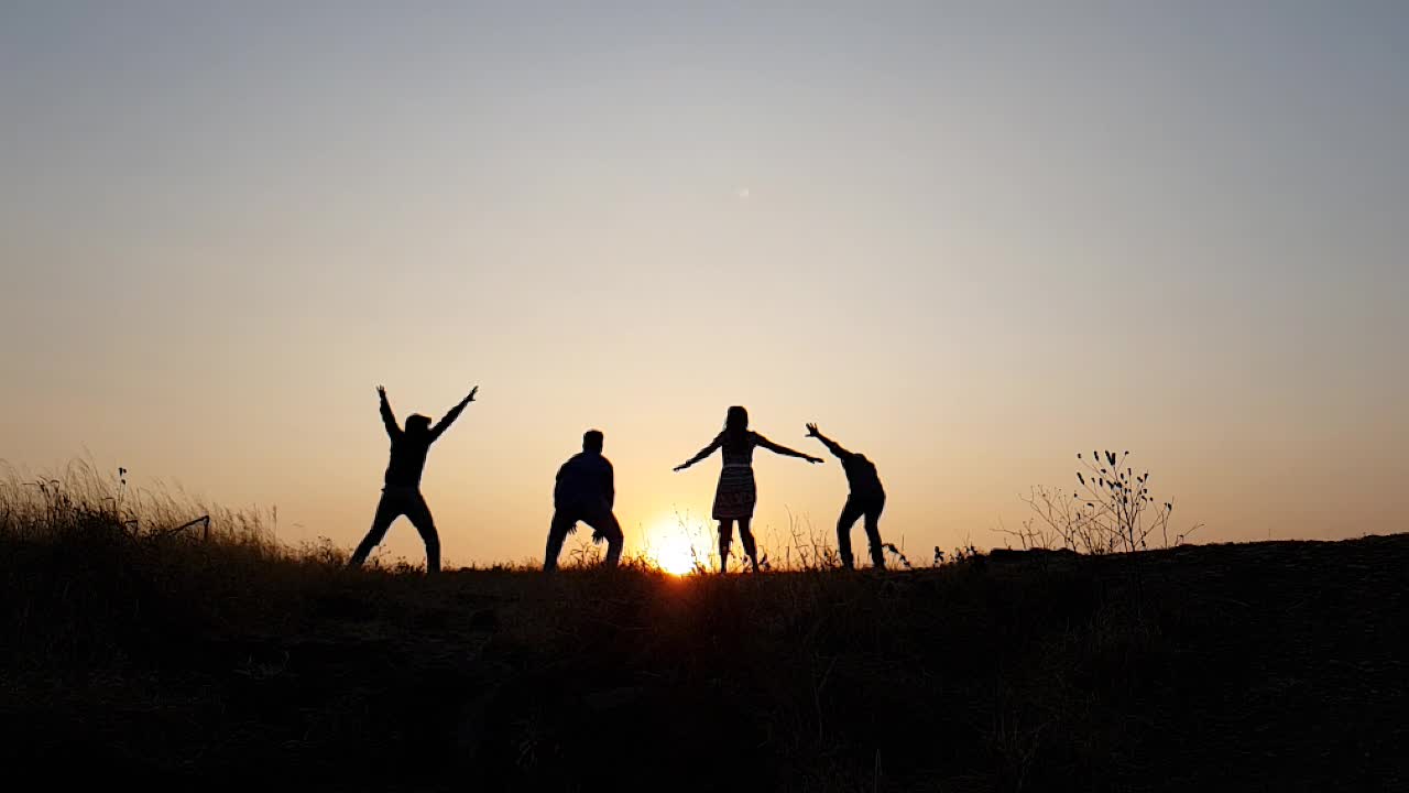 Silhouetted group of people jumping up during sunset in slow motion
