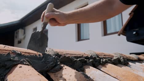 builder repairs terracotta tiled wall with sand, cement and trowel