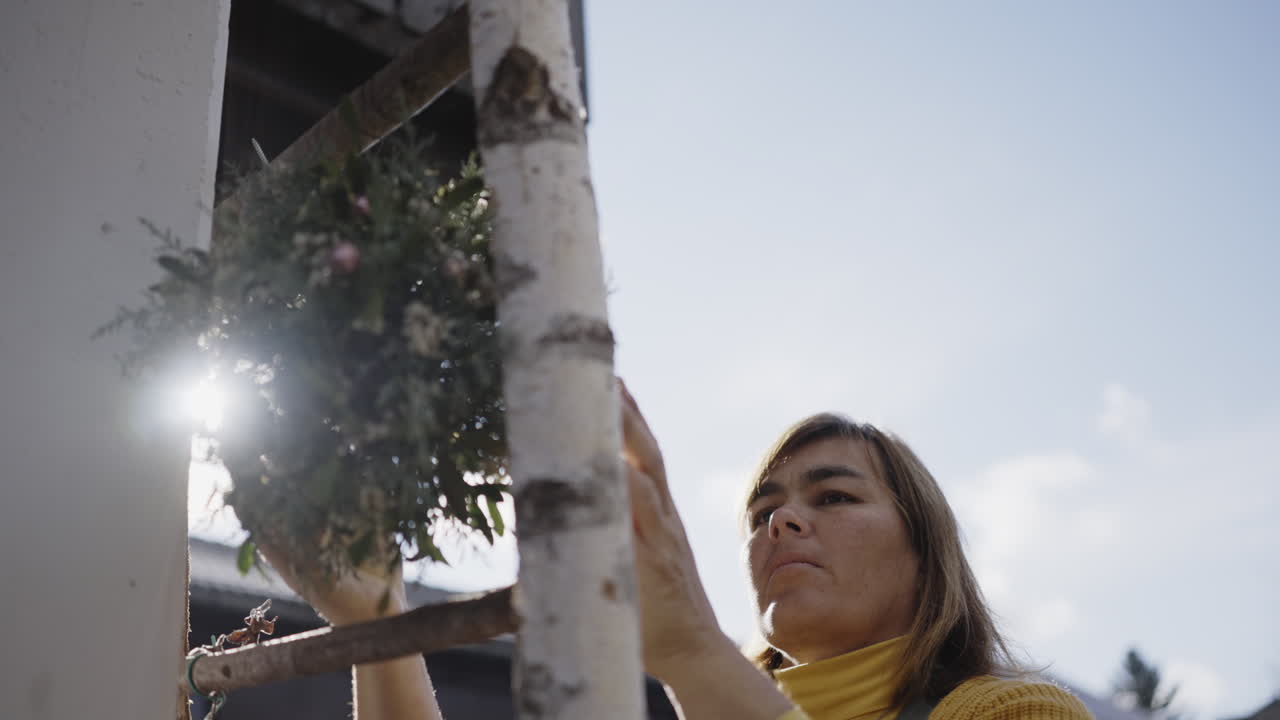 Woman Decorating with Wreath on a Ladder