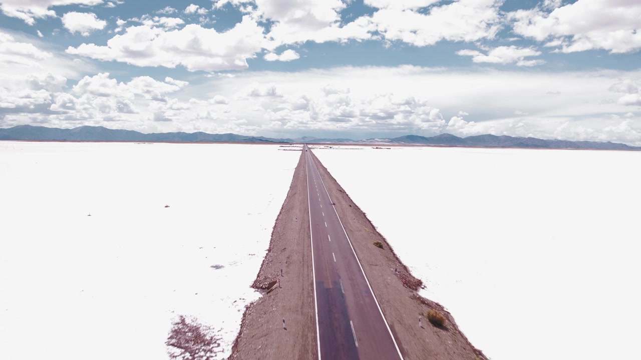 4K drone aerial view of Salinas Grandes in Jujuy, Argentina. One of the largest salt flats in the country, with endless white salt plains crossed by a road through the high altitude Andean Puna.