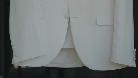 detailed close-up of a white suit jacket hanging, ready for the groom to wear for the wedding ceremony