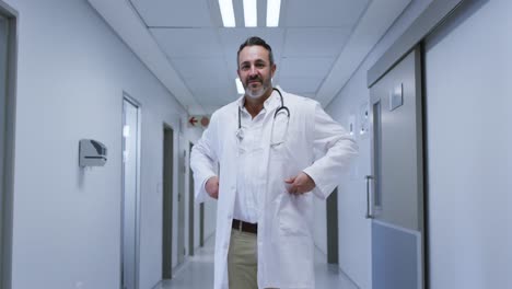 Portrait-of-smiling-caucasian-male-doctor-wearing-lab-coat-standing-in-hospital-corridor