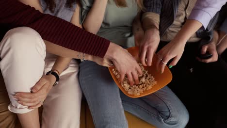 male and female hands grabbing popcorn while sitting on a sofa at home