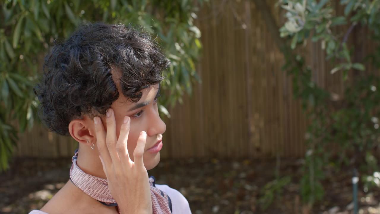 Touching face and looking away thoughtfully, non binary person contemplating outdoors