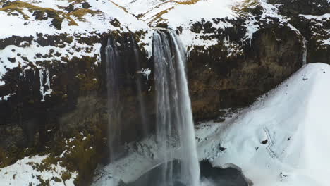 aerial view of birds circling a waterfall, in snowy iceland - rising, drone shot