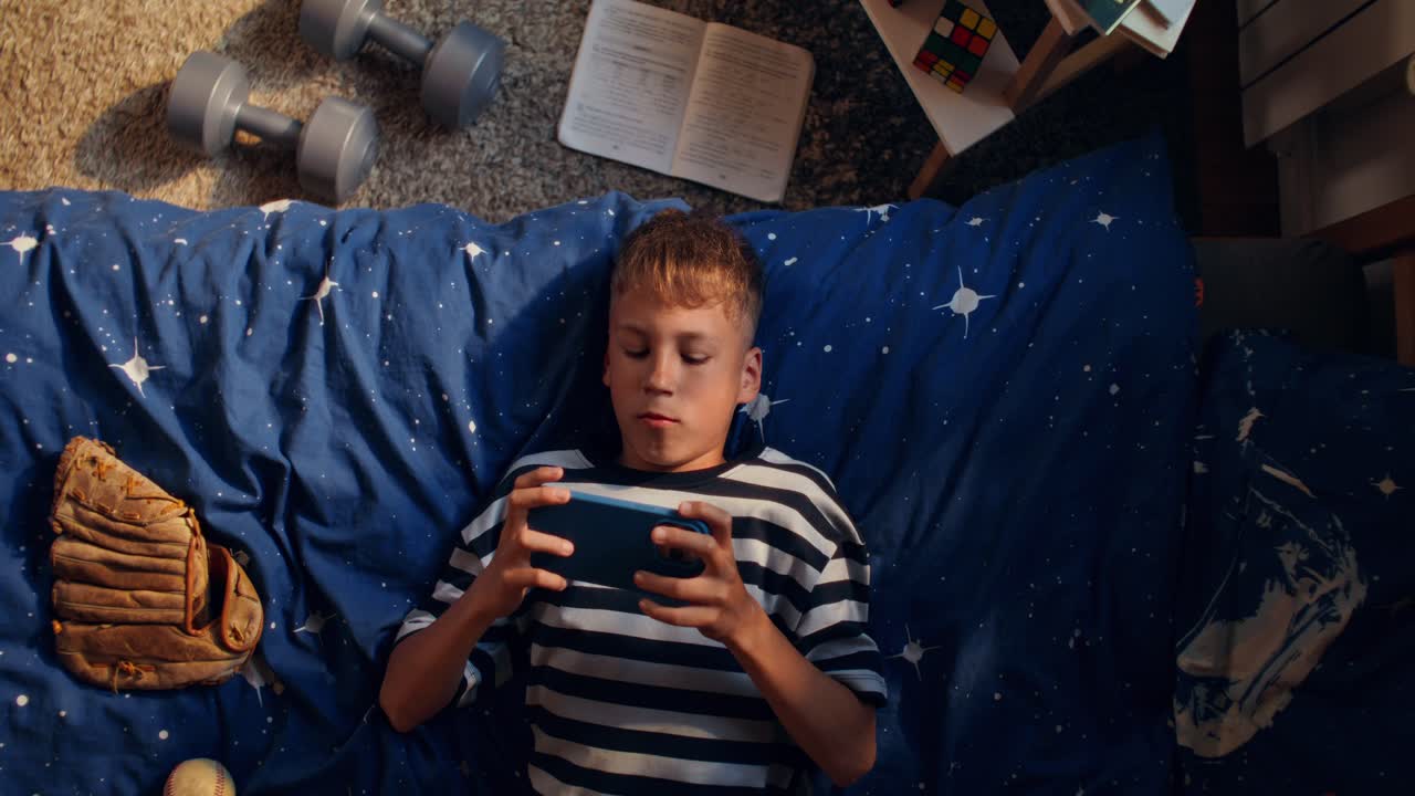 Teenage boy playing games on phone in his bedroom