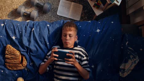 teenage boy playing games on phone in his bedroom