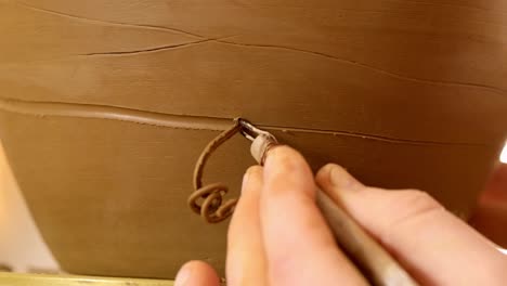 crafting intricate designs: a close-up of hand-carving patterns into wet clay using a sculpting tool for artisans and pottery enthusiasts