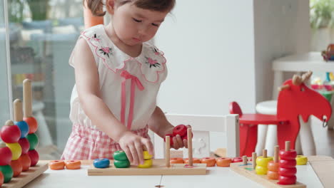 lovely child girl sorting colorful rings by color and stack on wooden poles with numbers