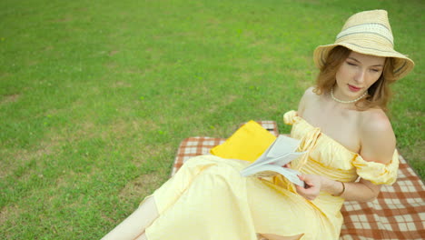 Attractive-Ukrainian-woman-in-yellow-dress-reading-on-picnic-blanket,-lies-down