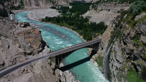 Wunderschöne-Luftdrohnenansicht-Eines-Wasserfalls-Und-Der-Ganish-Brücke-über-Den-Hunza-Fluss-In-Den-Bergen-Pakistans
