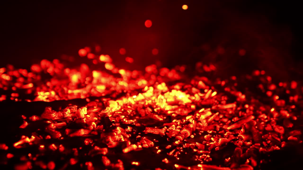 Blowing air on the burned charcoal. The pieces of burnt wood start to glow red and smoke goes up. Close up.