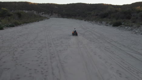 Drone-shot-follow-of-a-man-riding-a-motorcycle-in-a-dusty-terrain