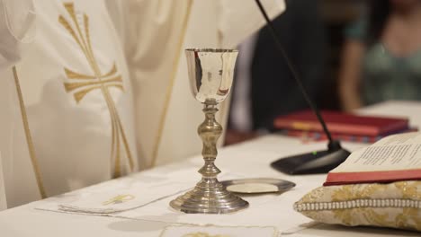 priest performing eucharistic ceremony with silver chalice, paten, and prayer book on the altar