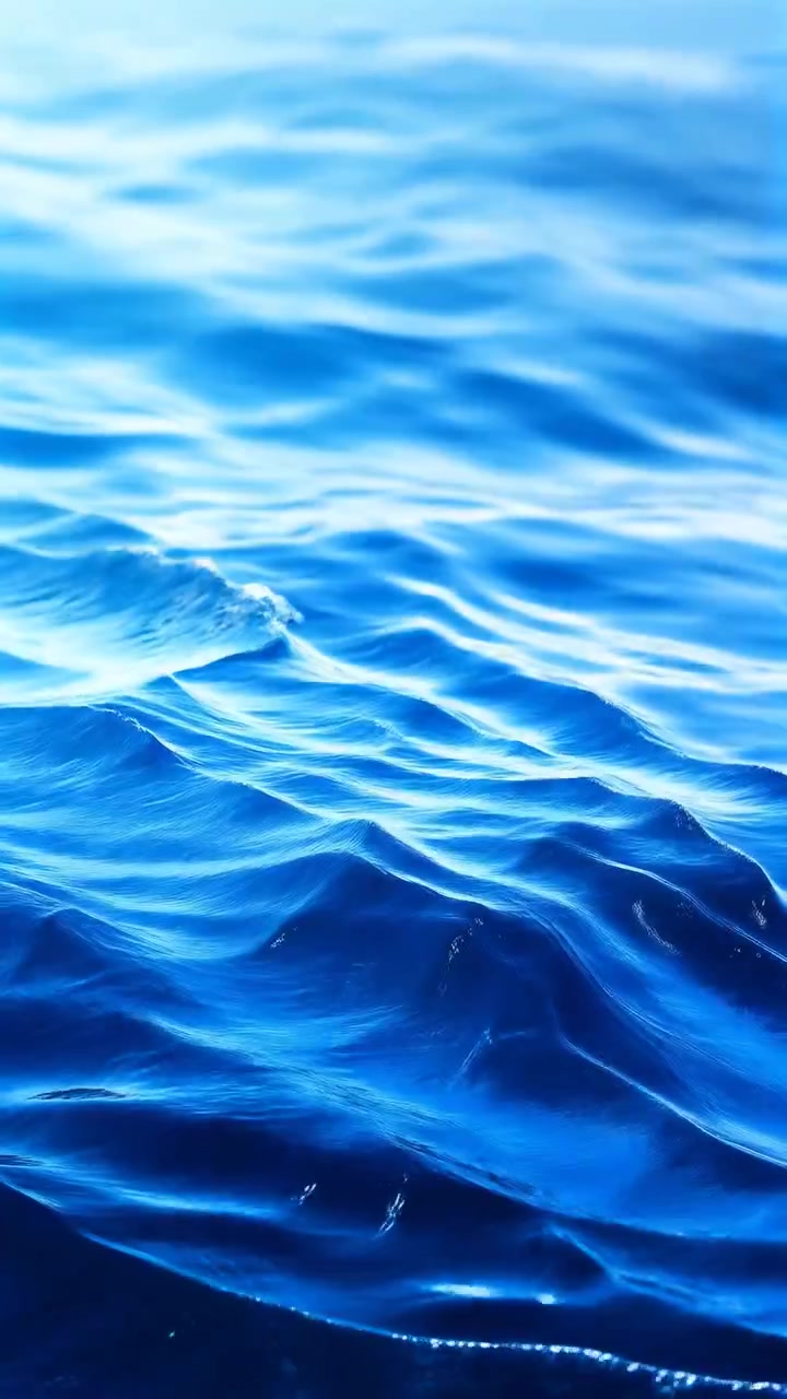 Oceaanoppervlak vanuit een laag standpunt met gelaagde golfbanden, glinsterende daglichtaccenten, diagonale rimpelstrepen, blauwe watertextuur, zachte diepte en een zuivere mariene abstractie.