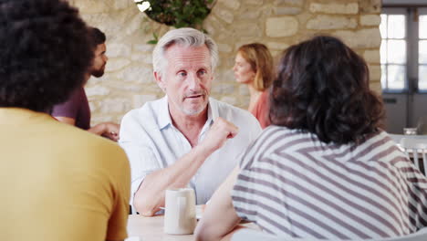 over shoulder view of senior man talking to friends at table in a restaurant, waist up