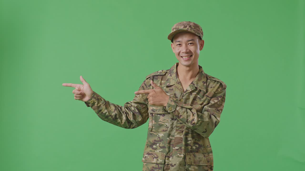 Asian Man Soldier Smiling And Pointing To Side While Standing In The Green Screen Background Studio