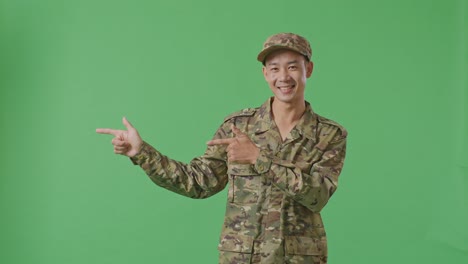 asian man soldier smiling and pointing to side while standing in the green screen background studio