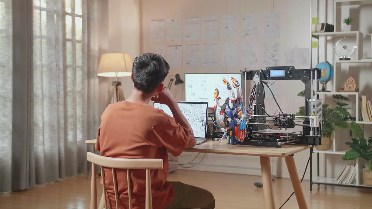 3d 프린팅으로 생각하고 집에서 노트북에서 사이보그 손을 디자인하는 동안 지표손가락을 올리는 소년의 뒷면