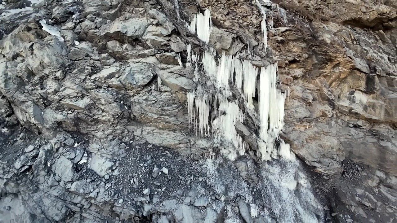 Frozen icicles cling to a textured rock face. A wintry landscape showcases the beauty of natural ice formations.