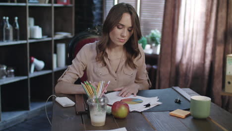 Concentrated-businesswoman-looking-documents-with-charts-and-diagrams-at-table