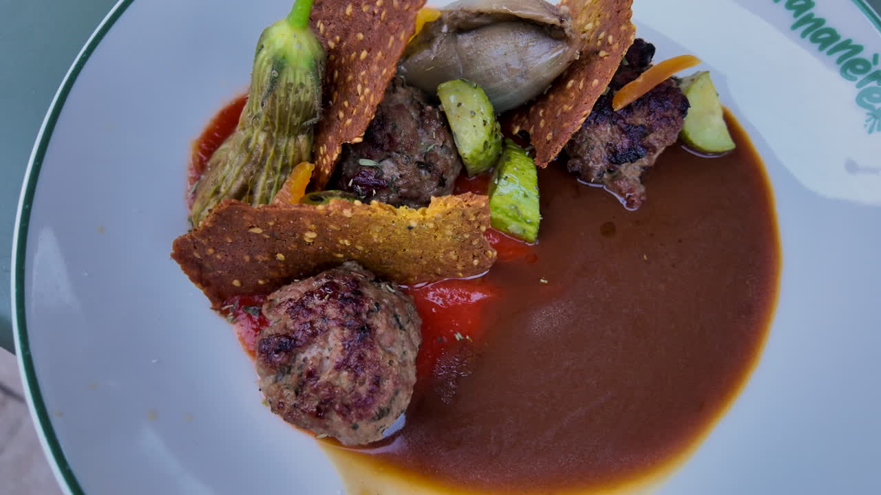 Close up of a combination of grilled meatballs, crispy sesame crackers, and a variety of vegetables