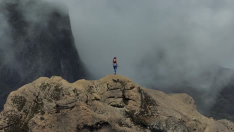 mujer de senderismo extremo en lo alto de la cresta mirando a las dramáticas montañas de niebla