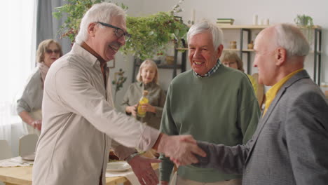 senior men shaking hands and talking at home party