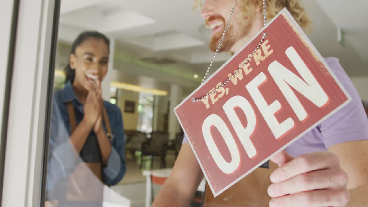 Happy diverse male and female baristas wearing black aprons opening up their coffee shop