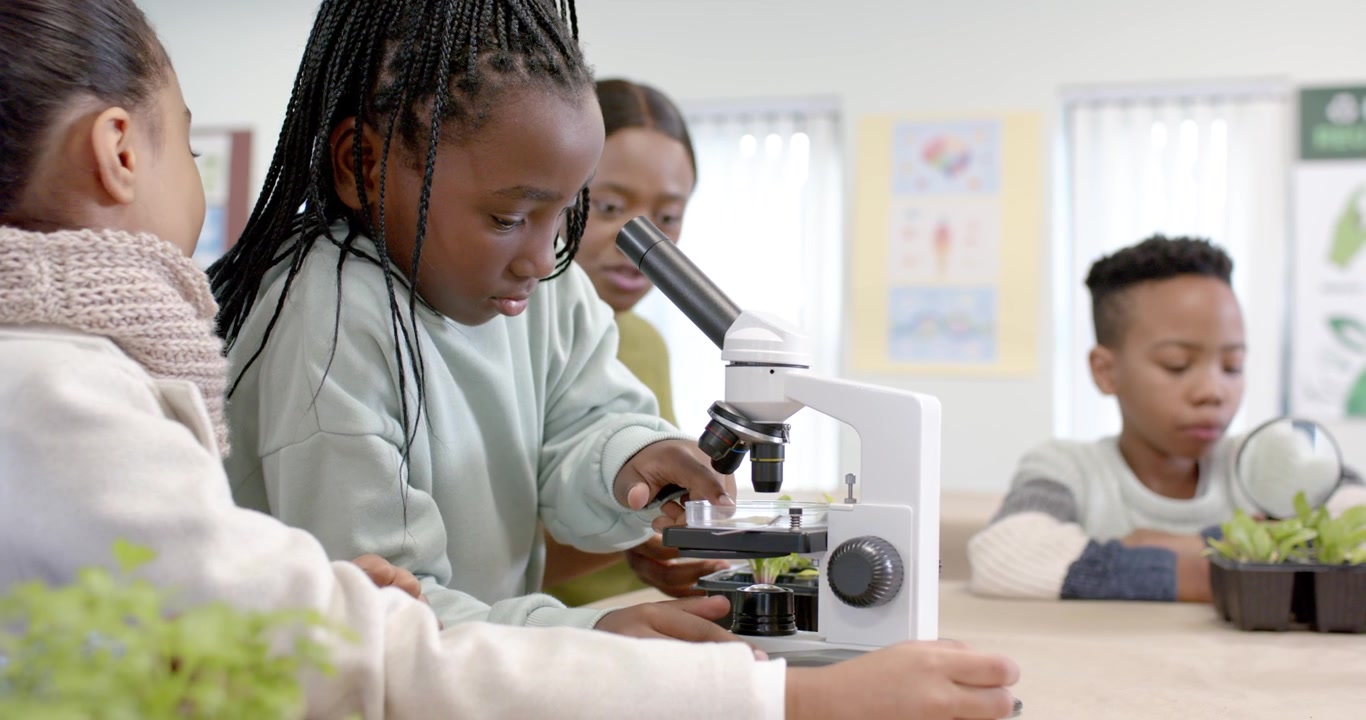 African American class watching braided girl operating microscope with teacher guiding near plants