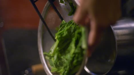 green vegetables being strained of water using metal strainer and tongs, filmed as vertical closeup slow motion shot