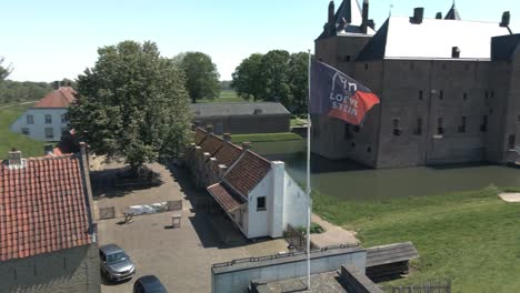 drone circling around flag of castle loevestein revealing unesco monument in the background on a bright sunny day in the netherlands