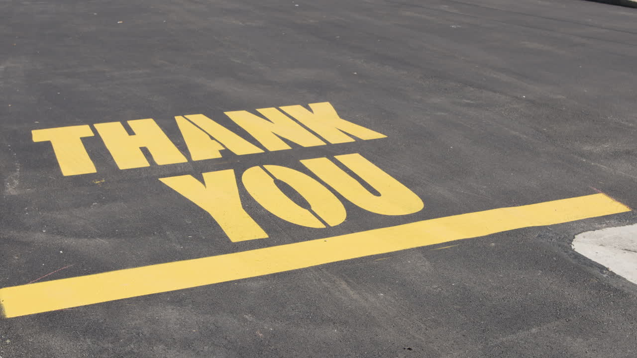 Still shot of Thank You message lettering in yellow paint on blacktop surface