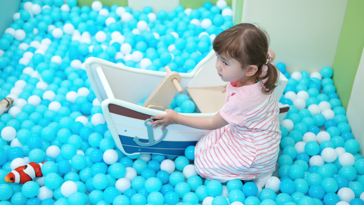 una niña linda jugando con bolas de plástico de varios colores en una gran piscina seca en el centro de juegos