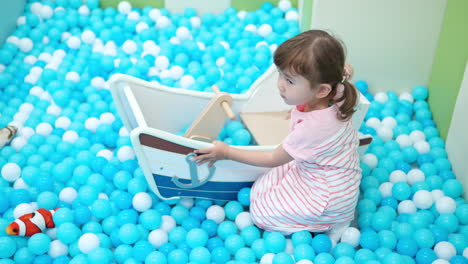 cute little girl playing on multi coloured plastic balls in big dry paddling pool in playing centre