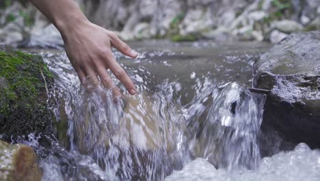 una mano toca el agua del arroyo. cámara lenta.