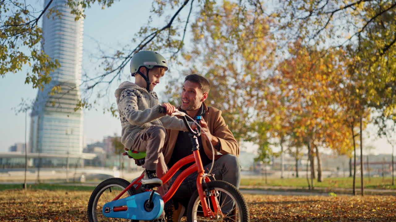 Father teaching his son to ride a bike in the park in the fall