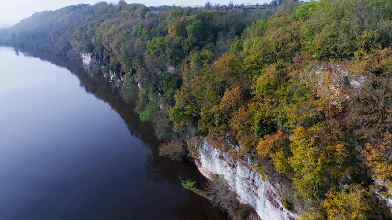 drone fpv volando a lo largo de un acantilado sobre un río con árboles en otoño, río dordogne - bac de sors en francia