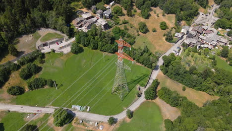 torre de transmisión con líneas de transmisión de alto voltaje en el campo cerca de la montaña y cabañas en morgex, val d'aosta, italia