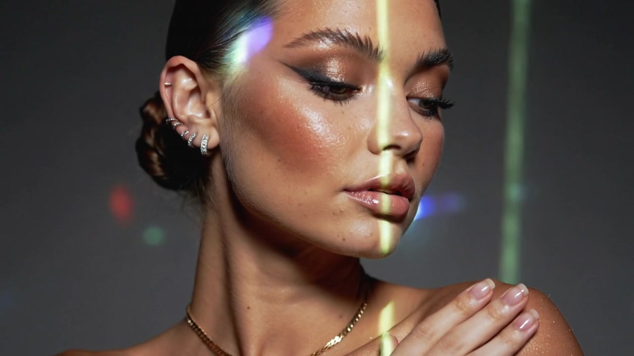 Modella che si gira, delineando la spalla con un trucco occhi alato in studio, mentre bagliori di luce spazzano via rivelando una catena.