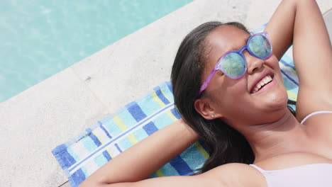 Alto-ángulo-De-Feliz-Chica-Afroamericana-Con-Gafas-De-Sol-Tomando-El-Sol-Junto-A-La-Piscina,-Espacio-Para-Copiar,-Cámara-Lenta