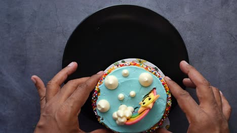 hands holding a decorated mini cake on a black plate