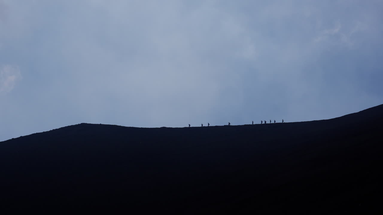 Silhouettes trekking on Mount Etna, conveying adventure against sky