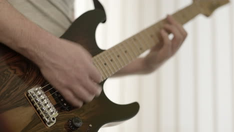 dof bajo primer plano de las manos de un músico masculino tocando una guitarra eléctrica de color marrón oscuro