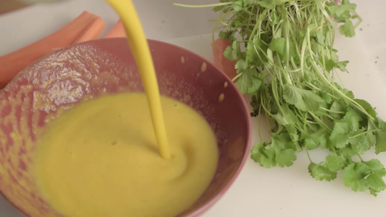 Pouring fresh carrot and coriander soup into a bowl medium top shot