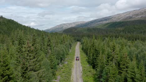 drone following suv with camper on rooftop driving offroad through evergreen forest in lomsdal-visten, norway