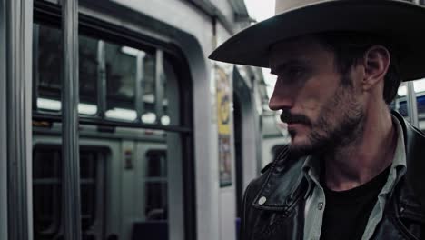 cowboy robusto en chaqueta de cuero y sombrero occidental sentado contemplativamente dentro del tren del metro, encarnando el contraste cultural rural urbano durante el viaje diario a través del sistema de transporte de la ciudad
