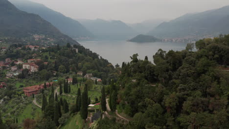 Flying-over-beautiful-mountain-road-and-old-city-towards-a-stunning-lake-in-Italy