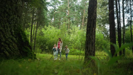 curious child holding object in hand while walking among trees with family in lush green forest, surrounded by tall trunks, thick foliage, and soft daylight